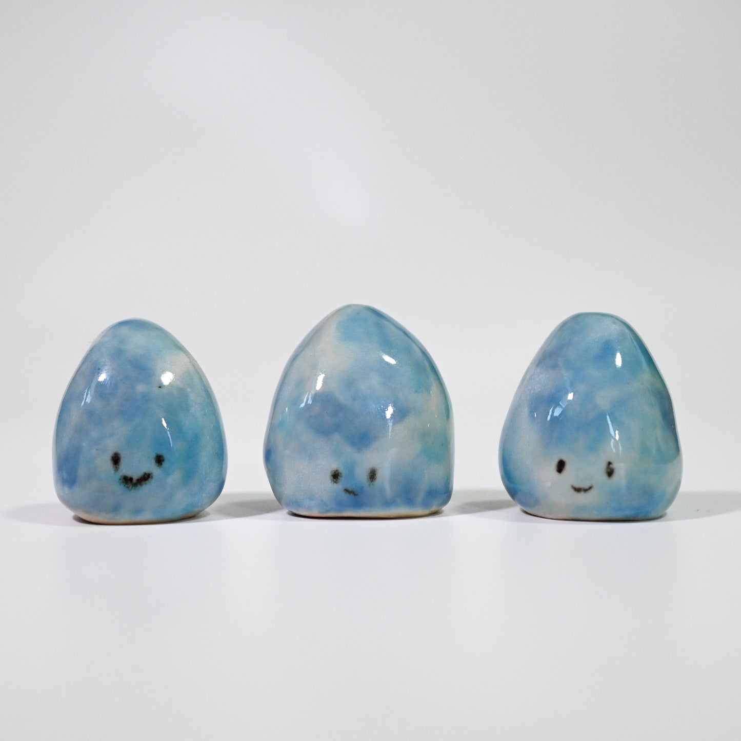 Three blue marbled stones with smiling faces on a white background